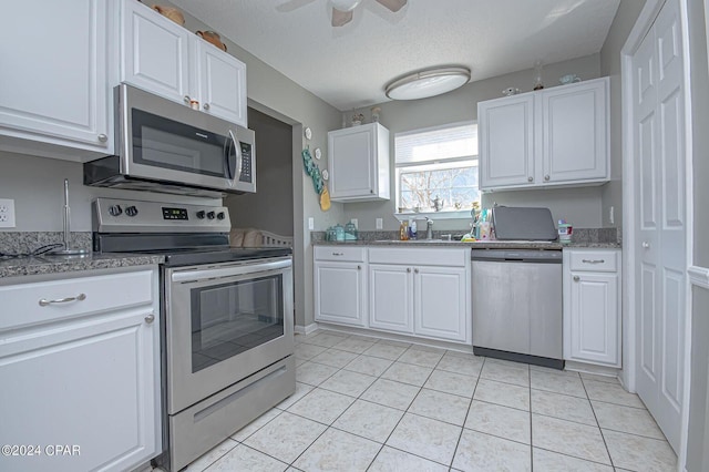 kitchen with a sink, light tile patterned floors, white cabinetry, and stainless steel appliances