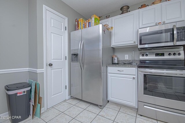 kitchen with white cabinets, light tile patterned flooring, appliances with stainless steel finishes, and a textured ceiling