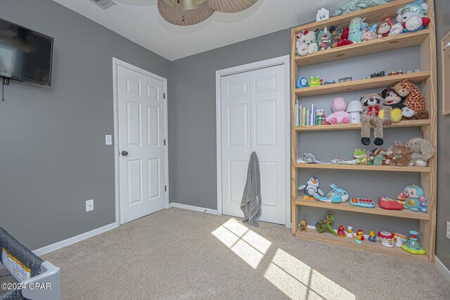 recreation room featuring visible vents, a textured ceiling, carpet floors, baseboards, and ceiling fan