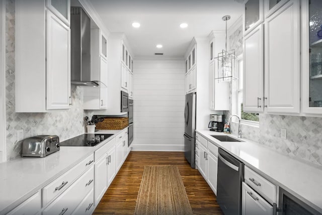 kitchen with white cabinets, black appliances, wall chimney range hood, and a sink