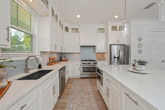 kitchen with premium range hood, a sink, light countertops, appliances with stainless steel finishes, and decorative light fixtures