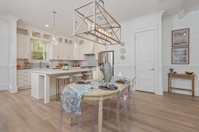 dining area with a chandelier, wainscoting, light wood-type flooring, and crown molding