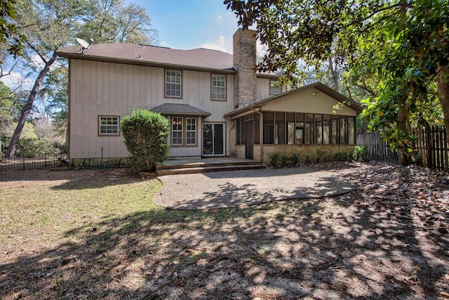 view of front of home featuring fence, a sunroom, a chimney, a front lawn, and a patio area