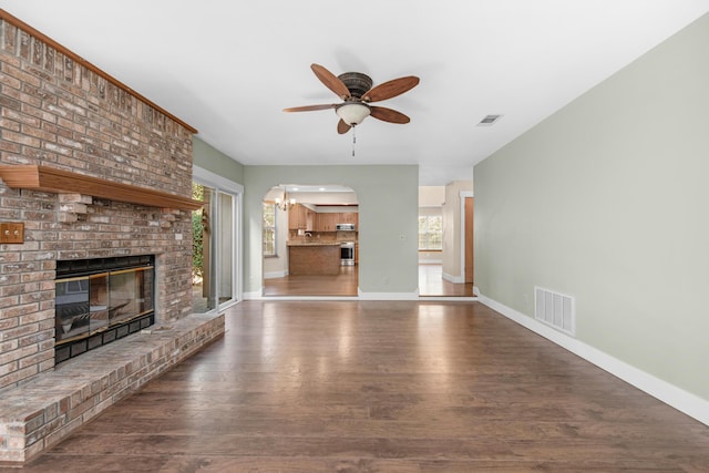 unfurnished living room featuring visible vents, ceiling fan with notable chandelier, a brick fireplace, and wood finished floors