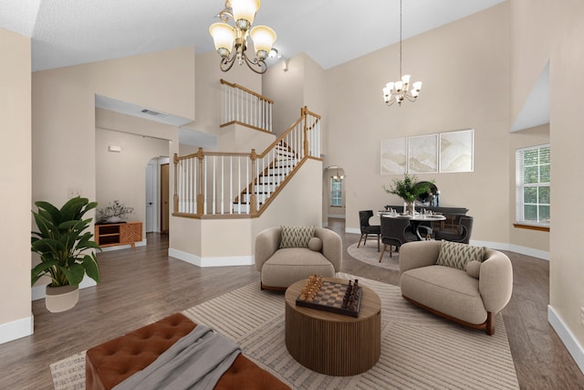 living room featuring stairway, wood finished floors, baseboards, high vaulted ceiling, and an inviting chandelier