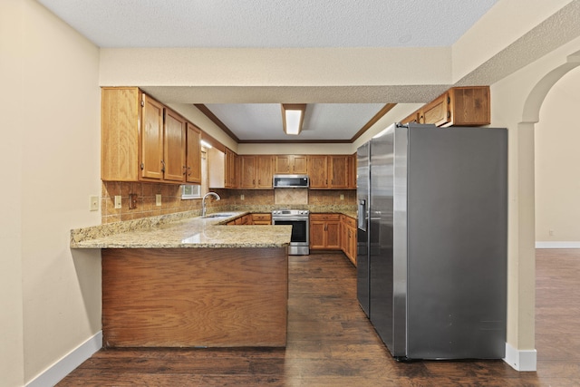 kitchen featuring tasteful backsplash, dark wood finished floors, a peninsula, stainless steel appliances, and a sink