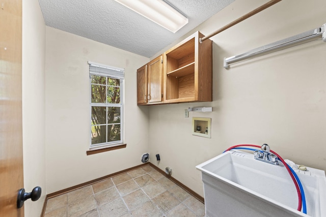 laundry room with hookup for a washing machine, baseboards, cabinet space, a sink, and a textured ceiling