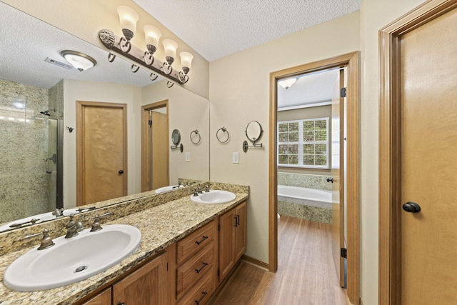 bathroom with a textured ceiling, a bath, wood finished floors, and a sink