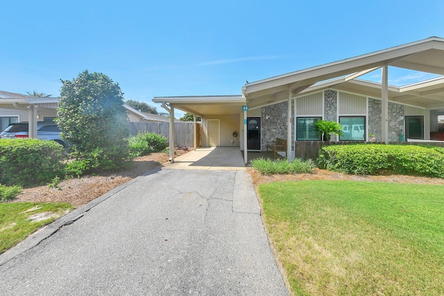 mid-century inspired home with aphalt driveway, stone siding, an attached carport, and a front yard