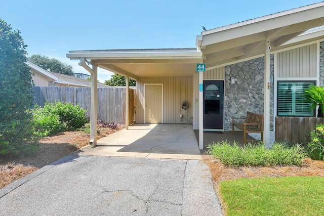 exterior space featuring stone siding, a carport, concrete driveway, and fence