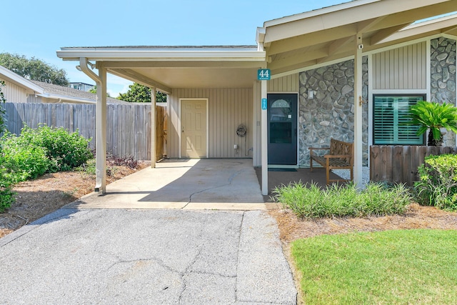 property entrance with stone siding, a carport, driveway, and fence