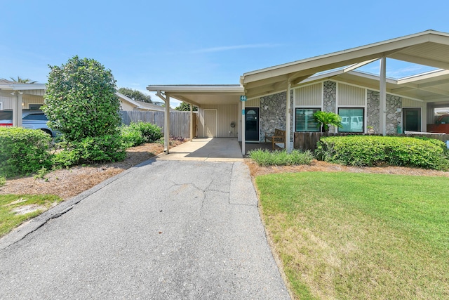 mid-century modern home featuring fence, aphalt driveway, a front yard, a carport, and stone siding