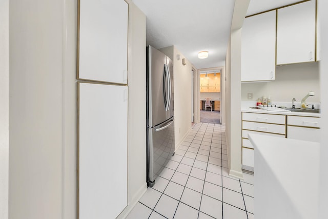 kitchen with baseboards, light countertops, light tile patterned floors, freestanding refrigerator, and white cabinets