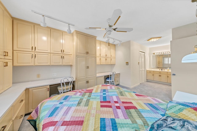 bedroom with light carpet, a ceiling fan, ensuite bath, and built in desk