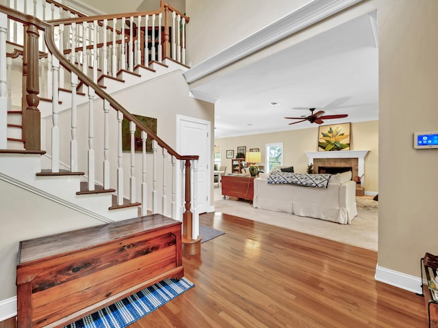 staircase featuring ornamental molding, a ceiling fan, wood finished floors, a fireplace, and baseboards