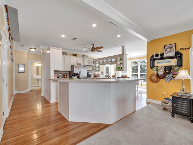 kitchen with a ceiling fan, light countertops, white cabinets, crown molding, and stainless steel fridge