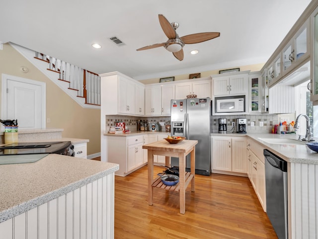 kitchen with light wood-type flooring, a sink, appliances with stainless steel finishes, light countertops, and ceiling fan