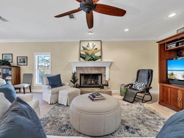 carpeted living room with a tiled fireplace, crown molding, visible vents, and ceiling fan