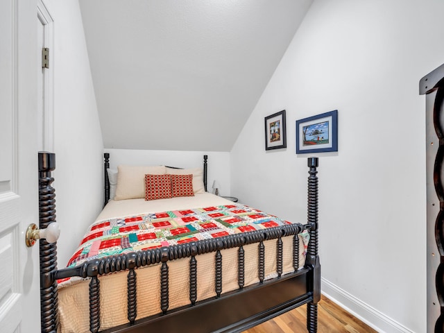 bedroom featuring baseboards, lofted ceiling, and wood finished floors