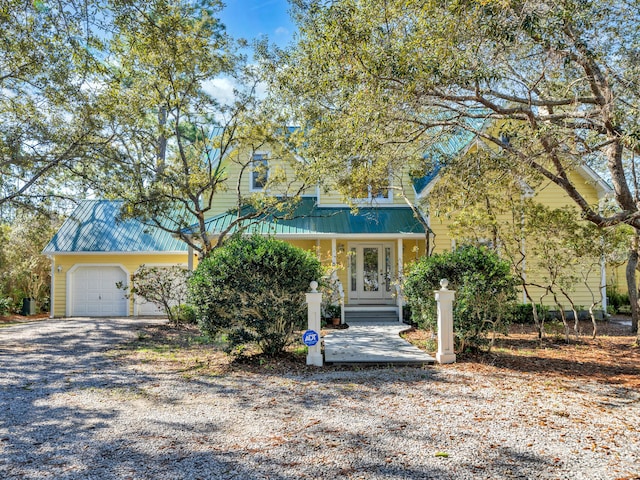 view of property hidden behind natural elements with metal roof, an attached garage, driveway, and french doors