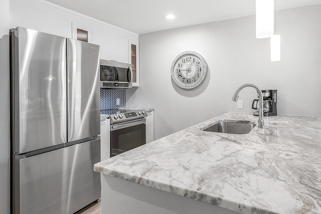 kitchen featuring white cabinetry, light stone countertops, stainless steel appliances, and a sink