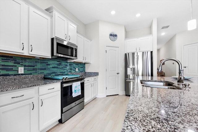 kitchen with visible vents, a sink, white cabinetry, dark stone counters, and appliances with stainless steel finishes