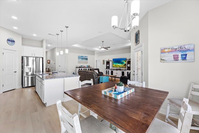 dining space featuring a raised ceiling, light wood-style flooring, ceiling fan with notable chandelier, recessed lighting, and baseboards