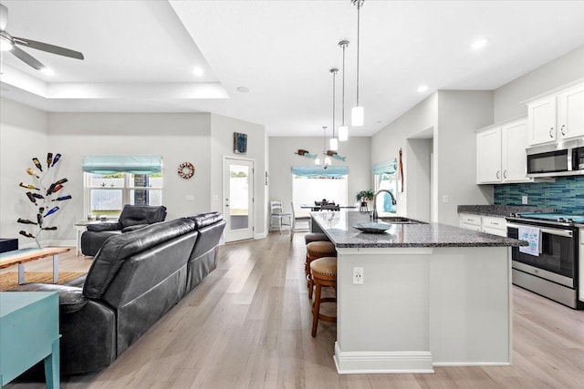 kitchen with open floor plan, dark stone counters, decorative backsplash, appliances with stainless steel finishes, and a sink