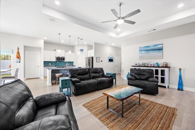 living room with a tray ceiling, visible vents, baseboards, and light wood-style floors