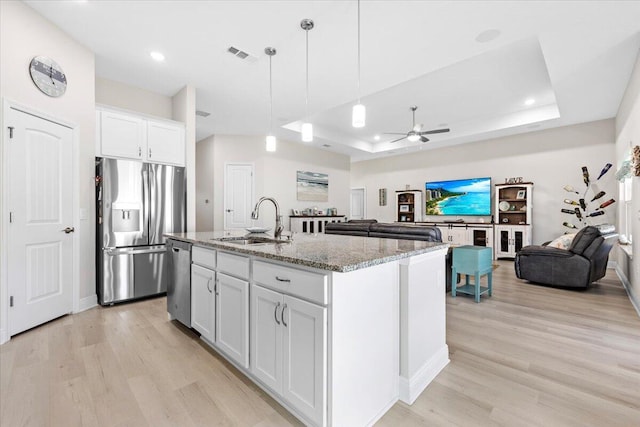 kitchen with visible vents, a sink, a tray ceiling, open floor plan, and appliances with stainless steel finishes