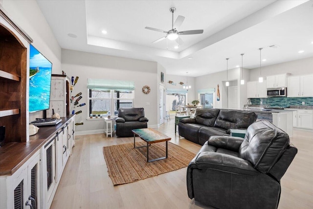 living room featuring visible vents, light wood-style flooring, a tray ceiling, recessed lighting, and baseboards