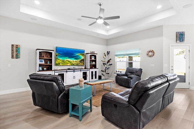 living area featuring baseboards, a raised ceiling, and light wood finished floors