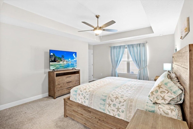 carpeted bedroom with ceiling fan, a raised ceiling, and baseboards