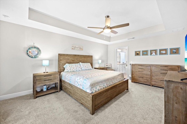 bedroom featuring visible vents, light carpet, a raised ceiling, ensuite bathroom, and baseboards