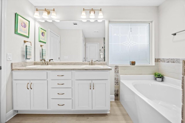 bathroom with double vanity, visible vents, a garden tub, and a sink