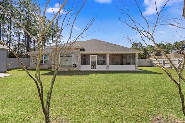 rear view of property featuring brick siding, a fenced backyard, a yard, and a sunroom