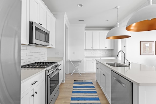 kitchen featuring visible vents, crown molding, light wood-style flooring, stainless steel appliances, and a sink