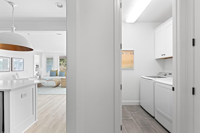 clothes washing area featuring light wood-type flooring, cabinet space, baseboards, and washing machine and clothes dryer