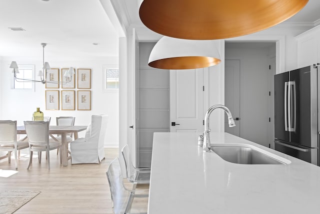 kitchen with light wood-style flooring, ornamental molding, a sink, freestanding refrigerator, and light countertops