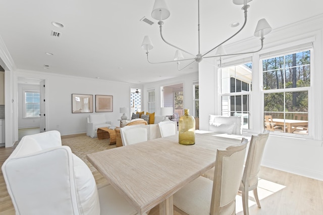 dining room featuring baseboards, visible vents, light wood-style flooring, ornamental molding, and a chandelier