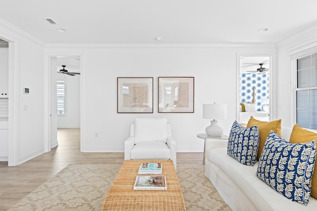 living area with visible vents, ornamental molding, wood finished floors, baseboards, and ceiling fan