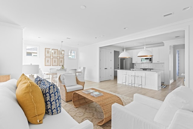 living room featuring light wood-type flooring, baseboards, visible vents, and crown molding