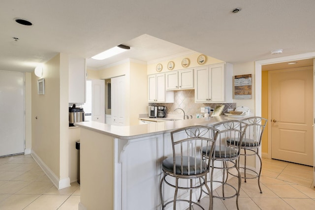 kitchen with tasteful backsplash, a breakfast bar area, light countertops, a peninsula, and a sink