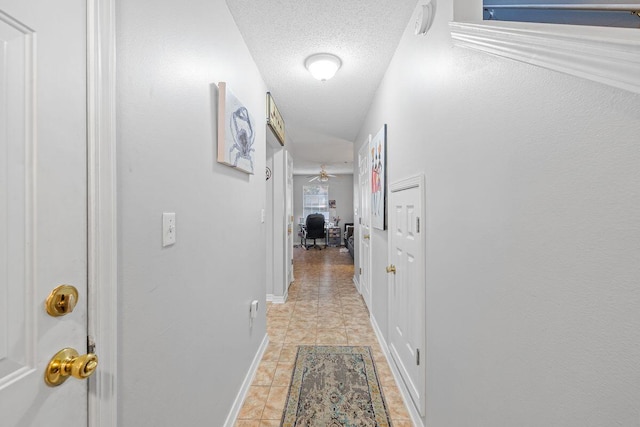 corridor featuring a textured ceiling and baseboards