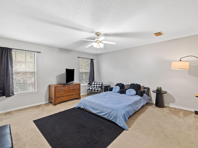 carpeted bedroom with visible vents, baseboards, a textured ceiling, and a ceiling fan