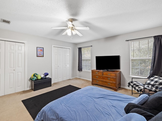 carpeted bedroom featuring visible vents, two closets, baseboards, a textured ceiling, and a ceiling fan