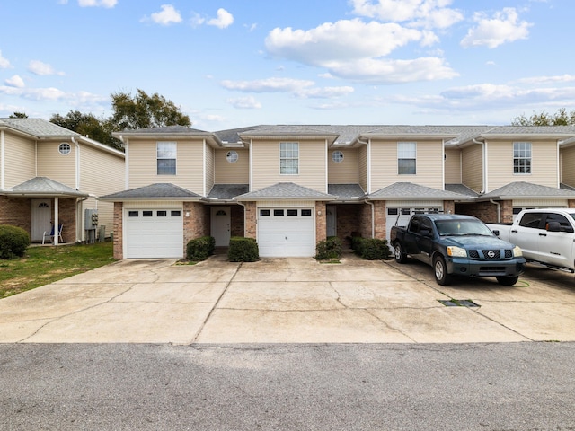 multi unit property featuring a garage, brick siding, driveway, and roof with shingles