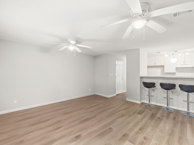 unfurnished living room with a ceiling fan, visible vents, baseboards, a textured ceiling, and light wood-type flooring