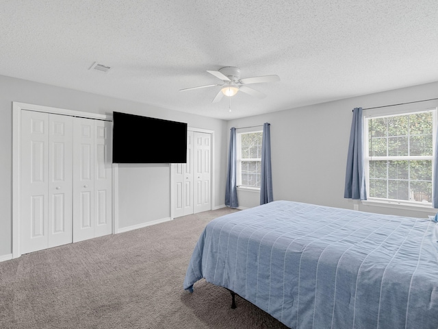 carpeted bedroom with visible vents, multiple windows, two closets, and a ceiling fan