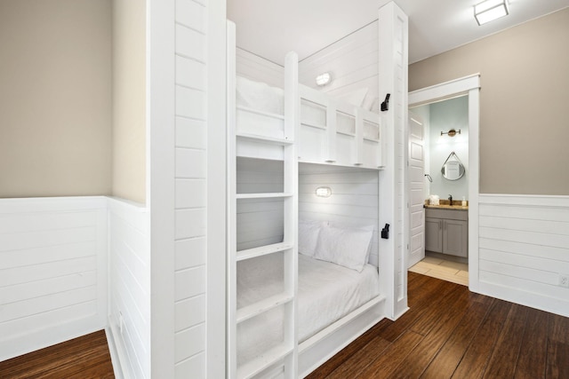 unfurnished bedroom featuring a wainscoted wall, connected bathroom, and dark wood-type flooring